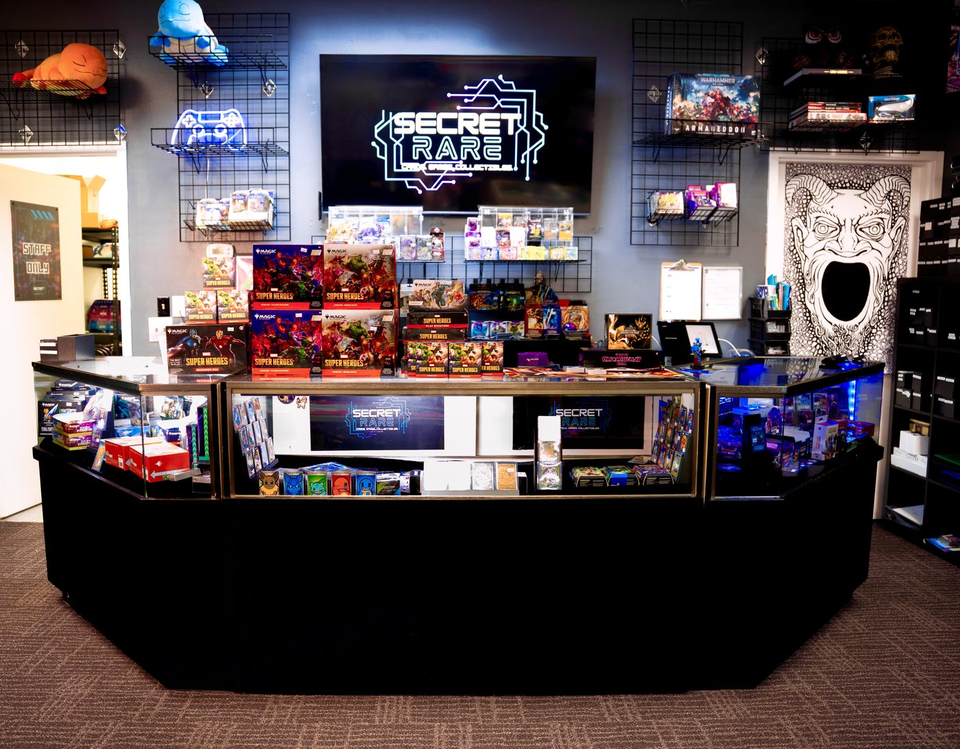 The Secret Rare Gaming front counter beneath the glowing logo screen, stacked with new releases and plushies